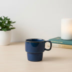 Blue ceramic mug on a light surface with a plant and candle in the background