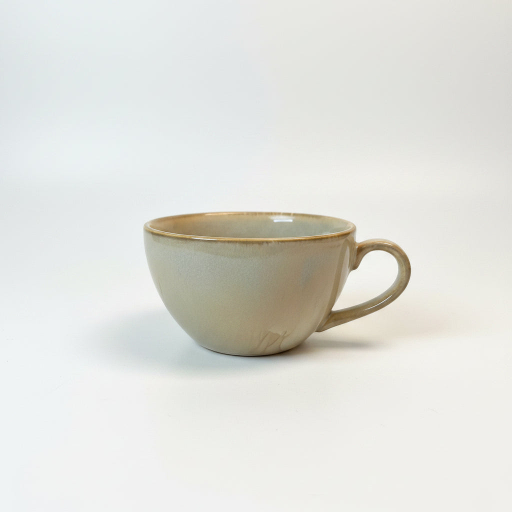 Hand holding a ceramic cup with a gold rim against a neutral background