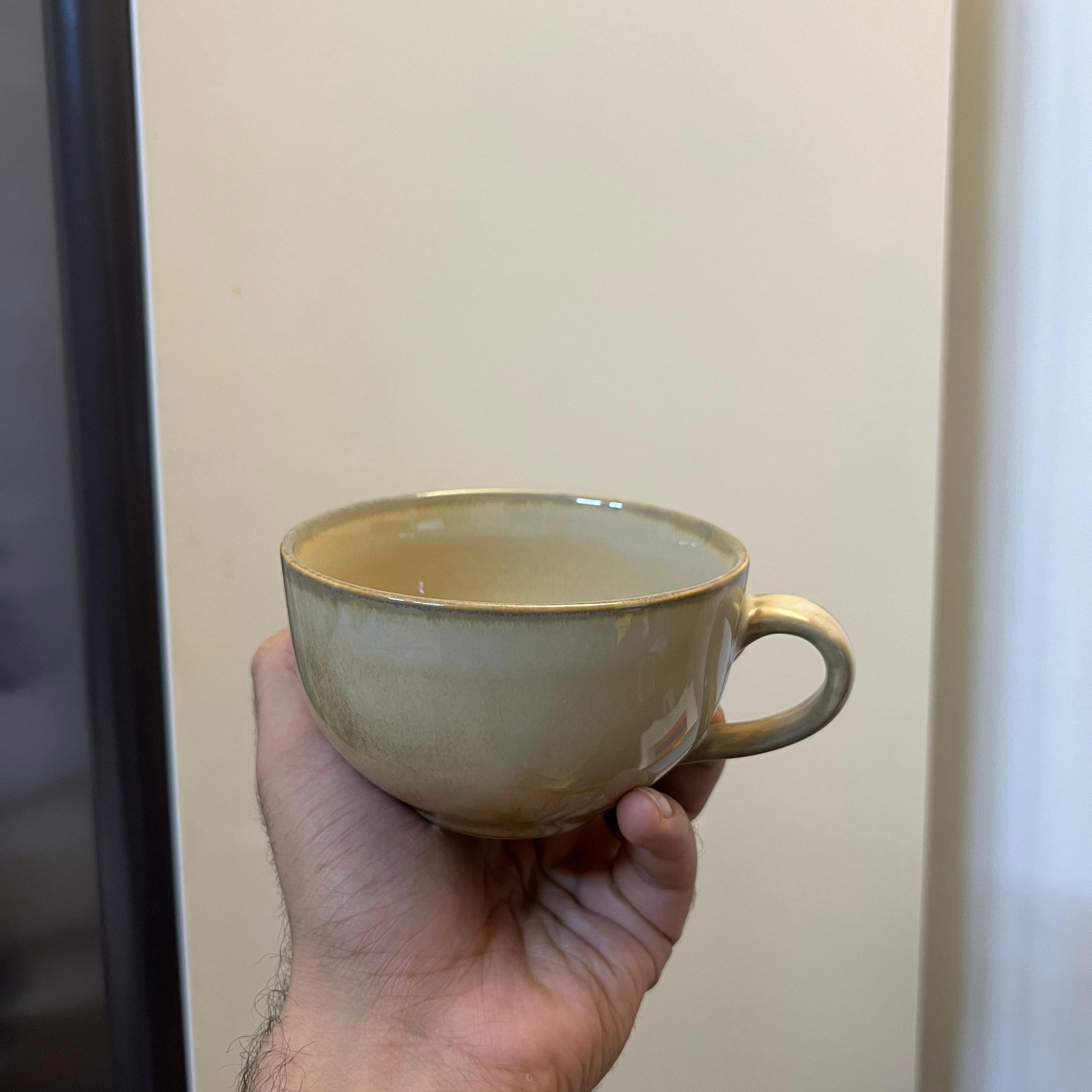 Hand holding a ceramic cup against a neutral background