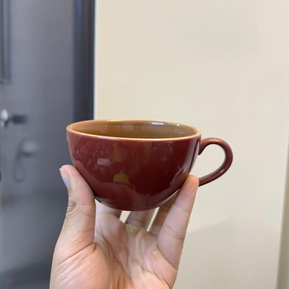 Hand holding a brown ceramic cup against a neutral background