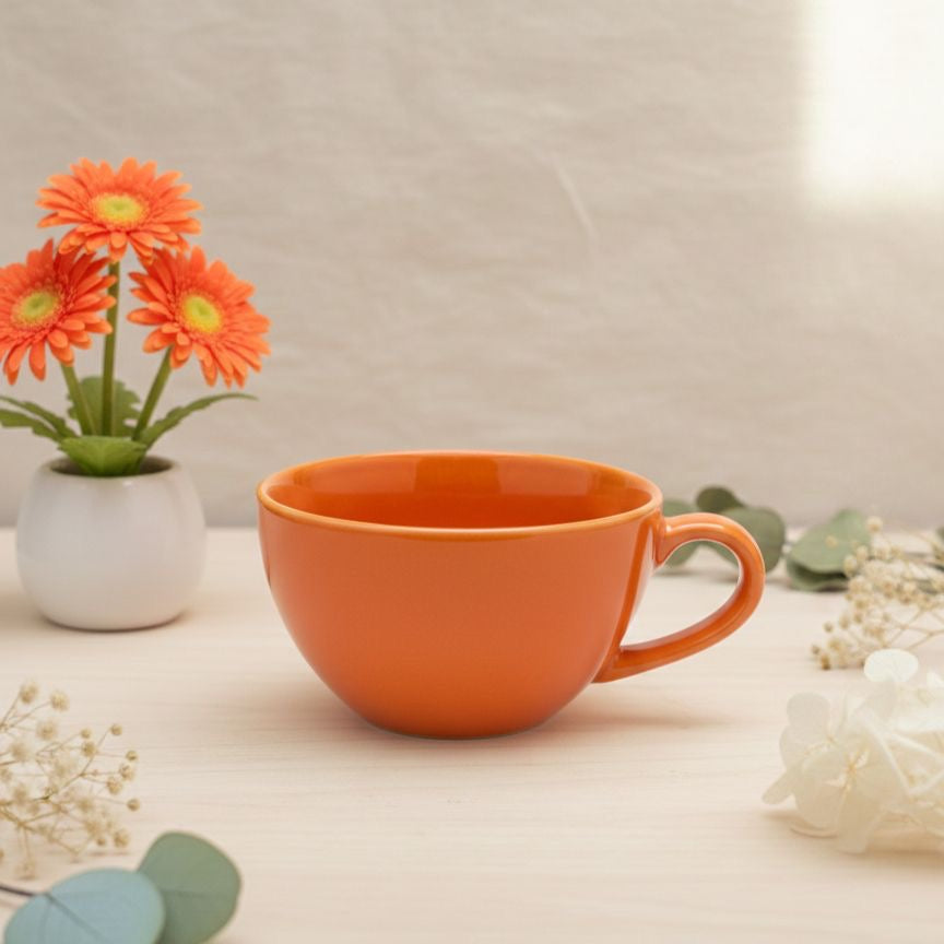 Orange mug on a light surface with decorative flowers and plants.